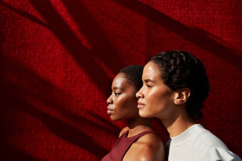 side view of women standing against red wall - fashion stock pictures, royalty-free photos & images