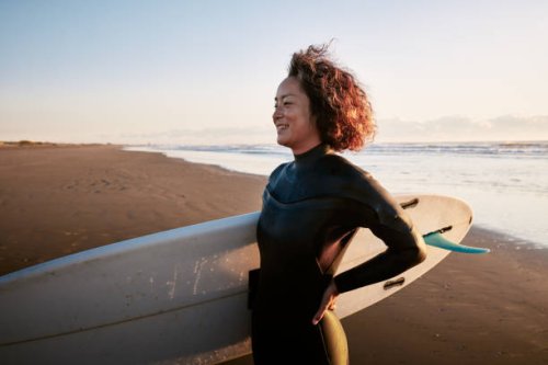 side view portrait of a woman standing in the surf with a surfboard under her arm. - travel stock pictures, royalty-free photos & images