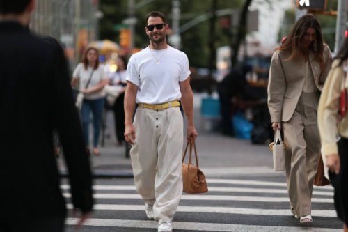 Simon Porte Jacquemus is seen wearing black Wayfarer sunglasses from Ray-Ban, a fine gold necklace with a rectangular pendant, an oversized white...