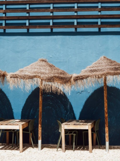 simple wooden tables and chairs with straw umbrellas outside the restaurant against blue wall - garden decoration stockfoto's en -beelden