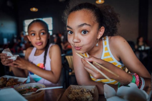 sisters eating takeout food with chopsticks in public park - junk food stock pictures, royalty-free photos & images