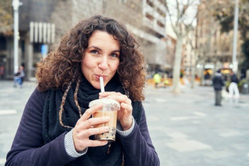 smiley woman drinking an iced coffee in the street - junk food stock pictures, royalty-free photos & images