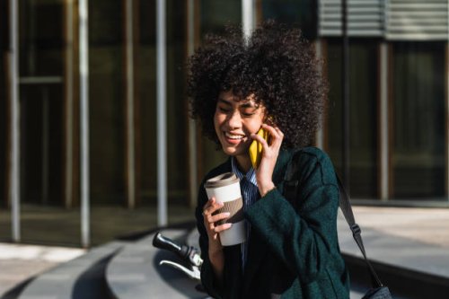 smiley woman using a mobile while drinking a take away coffee - junk food stock pictures, royalty-free photos & images