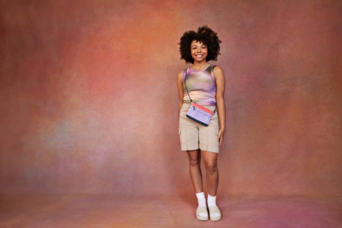 smiling afro teenage girl with sling bag standing against brown backdrop - fashion stock pictures, royalty-free photos & images