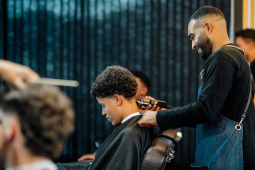 smiling barber trimming a customer's hair in a busy barber shop - hairstyle stock pictures, royalty-free photos & images