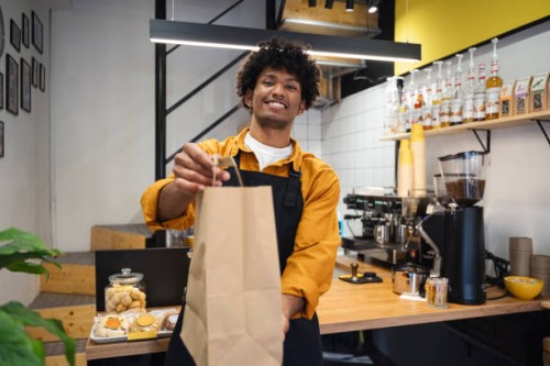 smiling barista holding takeaway bag at coffee shop - junk food stock pictures, royalty-free photos & images