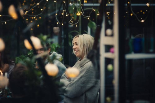 smiling blond young woman sitting amidst friends at dining table in back yard during garden party - garden decoration stock pictures, royalty-free photos & images