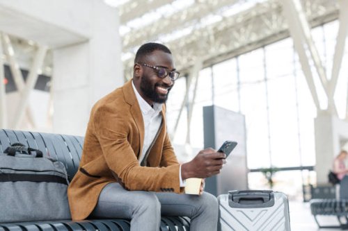 smiling businessman using smart phone in station departure lounge - travel stock pictures, royalty-free photos & images