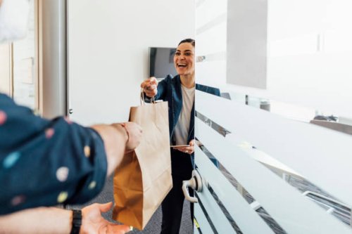 smiling businesswoman taking food delivery in office - junk food stock pictures, royalty-free photos & images