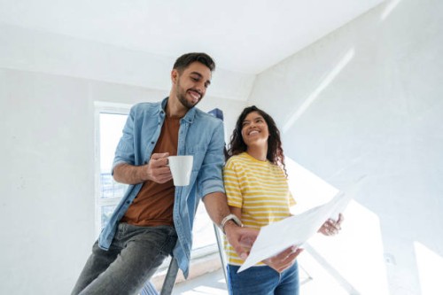 smiling couple having discussion over blueprint for renovation in new home - home decoration stockfoto's en -beelden