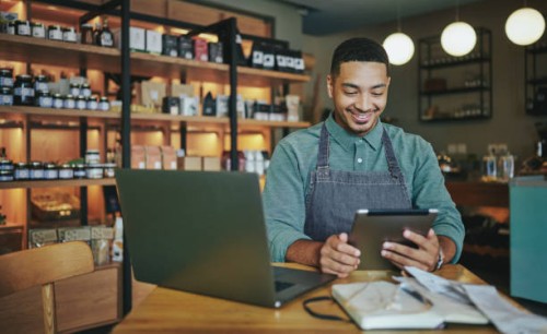 smiling deli manager working on a tablet and laptop in his shop - home decoration stock pictures, royalty-free photos & images