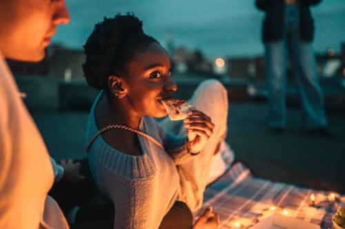smiling female eating pizza by friend on rooftop at night - junk food stock pictures, royalty-free photos & images