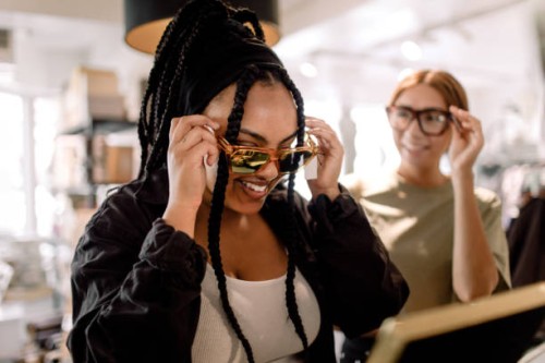 smiling female friends trying eyewear while talking at fashion store - fashion stock pictures, royalty-free photos & images