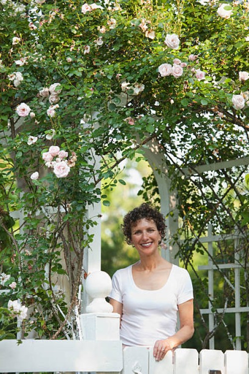 smiling hispanic woman standing underneath trellis - garden decoration stock-fotos und bilder