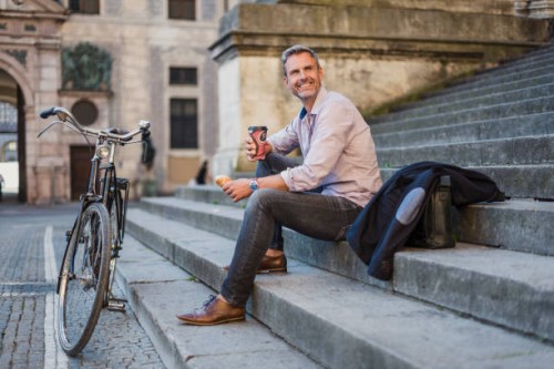 smiling man sitting on stairs with takeaway coffee in the city - junk food stock pictures, royalty-free photos & images