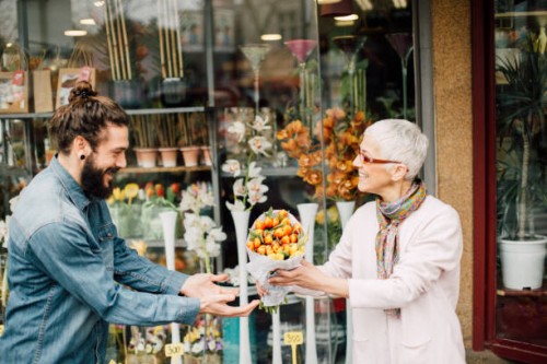 smiling man taking a flower bouquet from a senior florist - garden decoration stock pictures, royalty-free photos & images