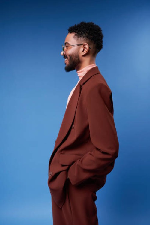 smiling man wearing brown blazer standing against blue background - fashion stock pictures, royalty-free photos & images