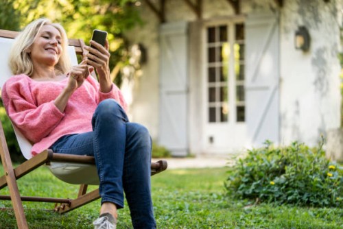 smiling mature woman using smartphone while sitting on deckchair - garden decoration photos et images de collection