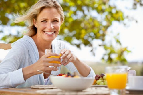 smiling mature woman with orange juice at breakfast table outdoors - food stock pictures, royalty-free photos & images