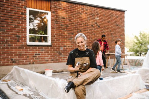 smiling mother looking at hand tool while family working in background during summer - home decoration stock pictures, royalty-free photos & images