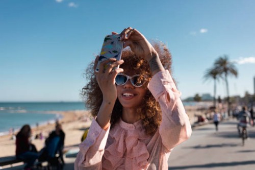 smiling stylish young woman taking a selfie at seaside promenade - fashion stock pictures, royalty-free photos & images