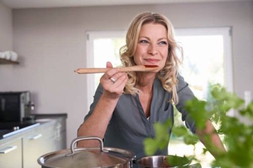 smiling woman cooking in kitchen tasting tomato sauce - food stock pictures, royalty-free photos & images