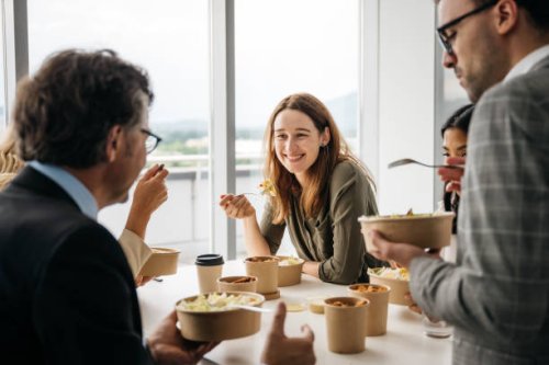 smiling woman enjoying takeaway lunch at work - junk food stock pictures, royalty-free photos & images
