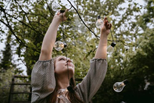 smiling woman hanging lighting equipment in yard during dinner party - garden decoration stock pictures, royalty-free photos & images