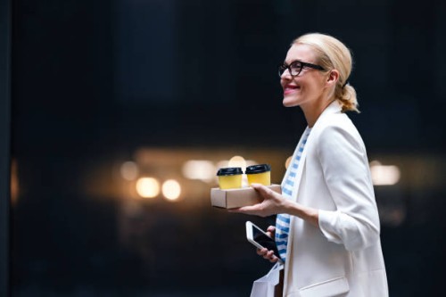 smiling woman holding two cups of coffee, mobile phone and shopping bags outdoors - junk food stock pictures, royalty-free photos & images