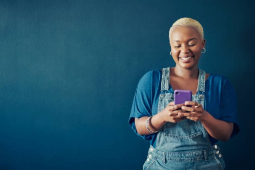 smiling woman in overalls texting on her phone against a blue background - fashion stock pictures, royalty-free photos & images
