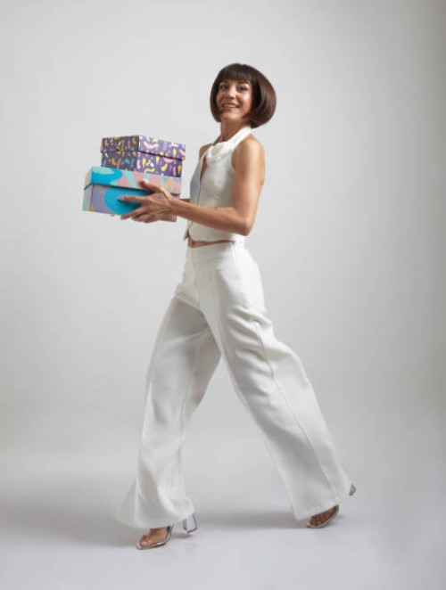 smiling woman in stylish white outfit with stubby hair walking on white background holding gift boxes in her hands. - fashion stock pictures, royalty-free photos & images