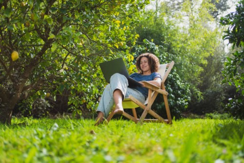 smiling woman looking at laptop while sitting on chair in permaculture garden - garden decoration photos et images de collection