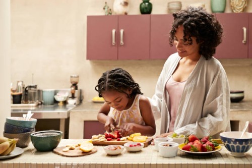 smiling woman standing by daughter cutting strawberry - home decoration stock-fotos und bilder