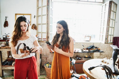 smiling woman using smartphone to take picture of shoe while shopping with friend in boutique - fashion stock pictures, royalty-free photos & images