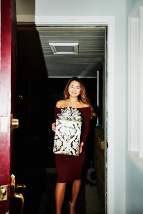 smiling woman walking into home with present for holiday party - fashion stock pictures, royalty-free photos & images