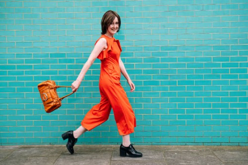 smiling woman wearing jumpsuit walking by brick wall - fashion stock pictures, royalty-free photos & images