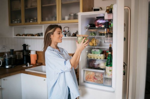 smiling woman with a container of brussels sprouts in front of open fridge in kitchen - food stock pictures, royalty-free photos & images