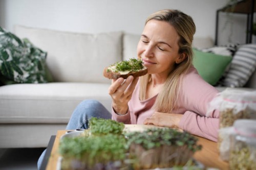 smiling woman with eyes closed enjoying sprouts on bread at home - food stock pictures, royalty-free photos & images
