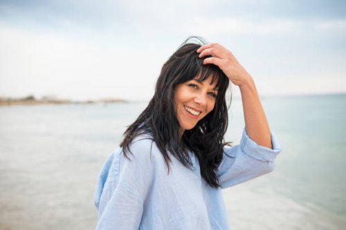 smiling woman with hand in hair at beach - hairstyle stockfoto's en -beelden