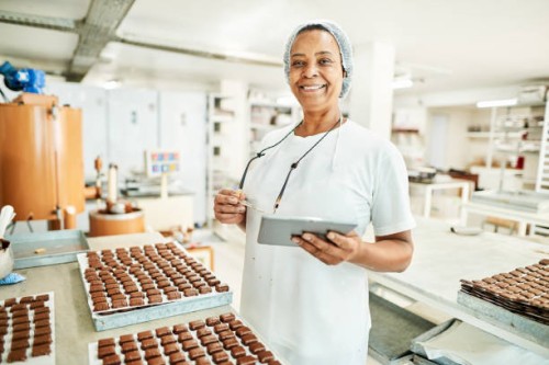 smiling worker using a digital tablet in a commercial chocolate making factory - food stock pictures, royalty-free photos & images