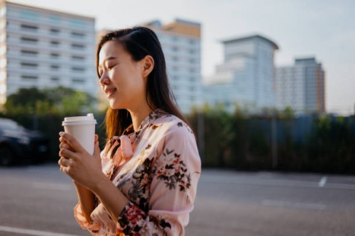smiling young asian woman enjoying a take away coffee in the morning - junk food stock pictures, royalty-free photos & images