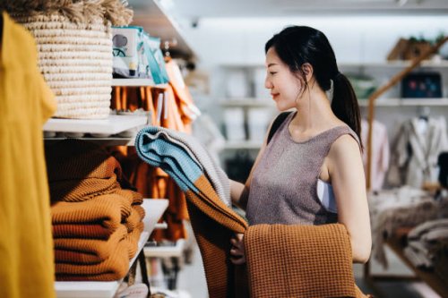 smiling young asian woman shopping for home decor and necessities in a homeware store, choosing for a blanket on a shelf - home decoration stock pictures, royalty-free photos & images