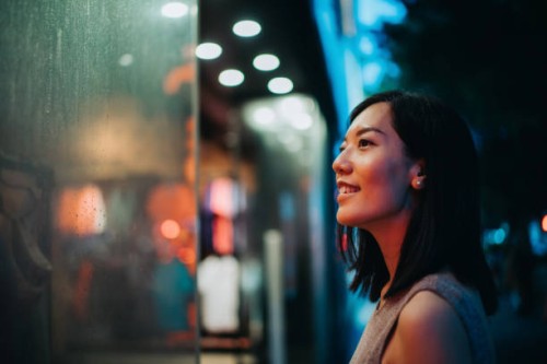 smiling young asian woman standing in front of a boutique and looking at shop window, shopping in city in the evening, with colourful neon lighting reflected on her - fashion stock pictures, royalty-free photos & images