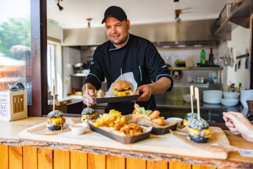 smiling young caucasian chef carring a tray with a delicious big meat burger at a small fast-food restaurant - junk food stock pictures, royalty-free photos & images