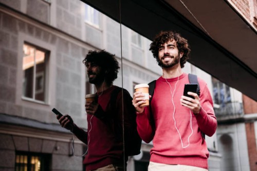 smiling young man with smart phone and coffee cup standing at footpath - junk food stock pictures, royalty-free photos & images