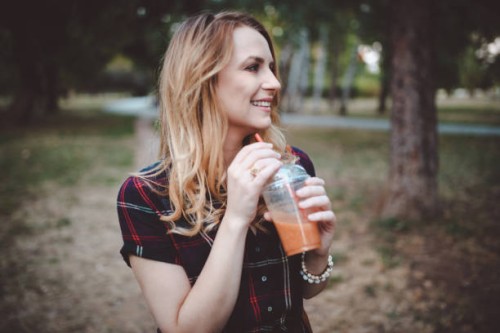 smiling young woman drinking smoothie in the public park - junk food stock pictures, royalty-free photos & images