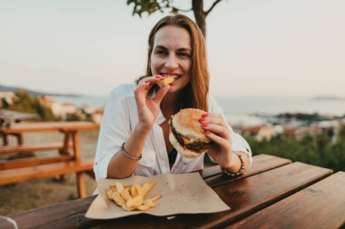 smiling young woman eating burger and fries during summer vacation in greece - junk food stock pictures, royalty-free photos & images