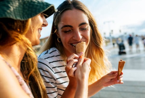 smiling young woman feeding ice cream to sister while spending enjoying in city - food stockfoto's en -beelden