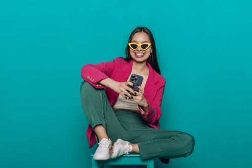 smiling young woman sitting on a chair chatting in via smartphone using the internet. - fashion stock pictures, royalty-free photos & images