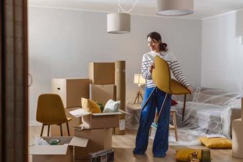 smiling young woman surrounded by boxes while moving, unpacking personal belongings - home decoration stock pictures, royalty-free photos & images